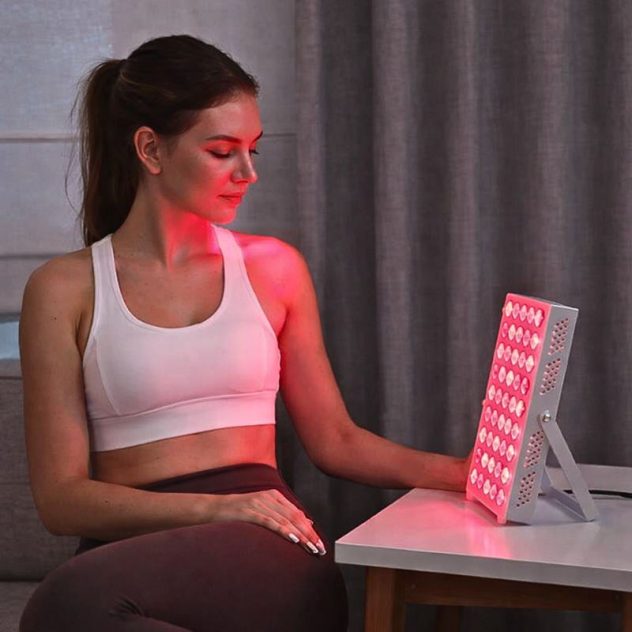 Girl using red light therapy panel on desk.