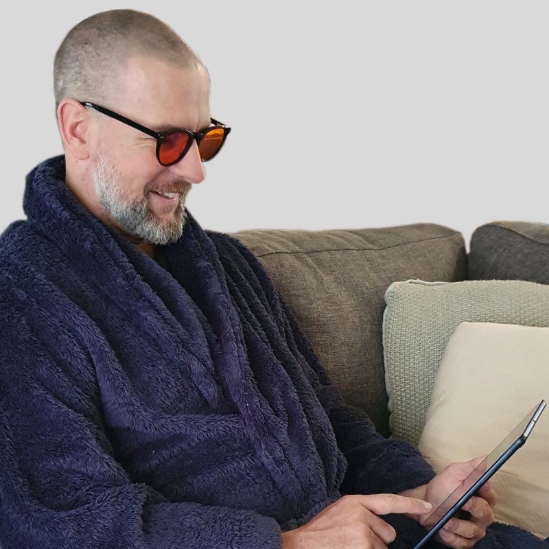Blue light sleep glasses worn by man smiling on tablet. Blue light sleep glasses worn by man smiling on tablet.
