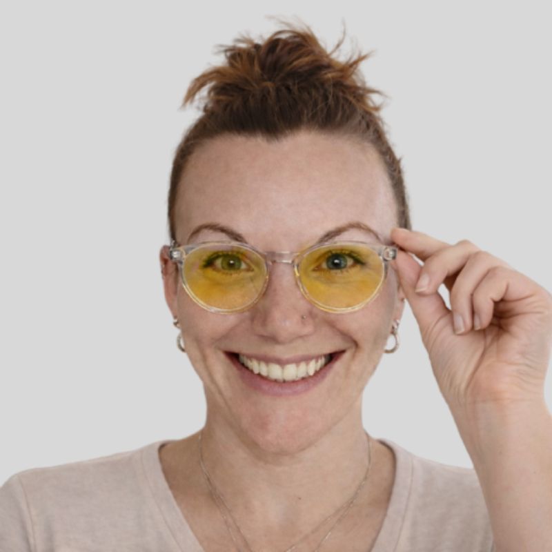 Woman wearing clear frame blue light blocking glasses with yellow lenses, shown in a sharp front-facing studio portrait. Woman wearing clear frame blue light blocking glasses with yellow lenses, shown in a sharp front-facing studio portrait.