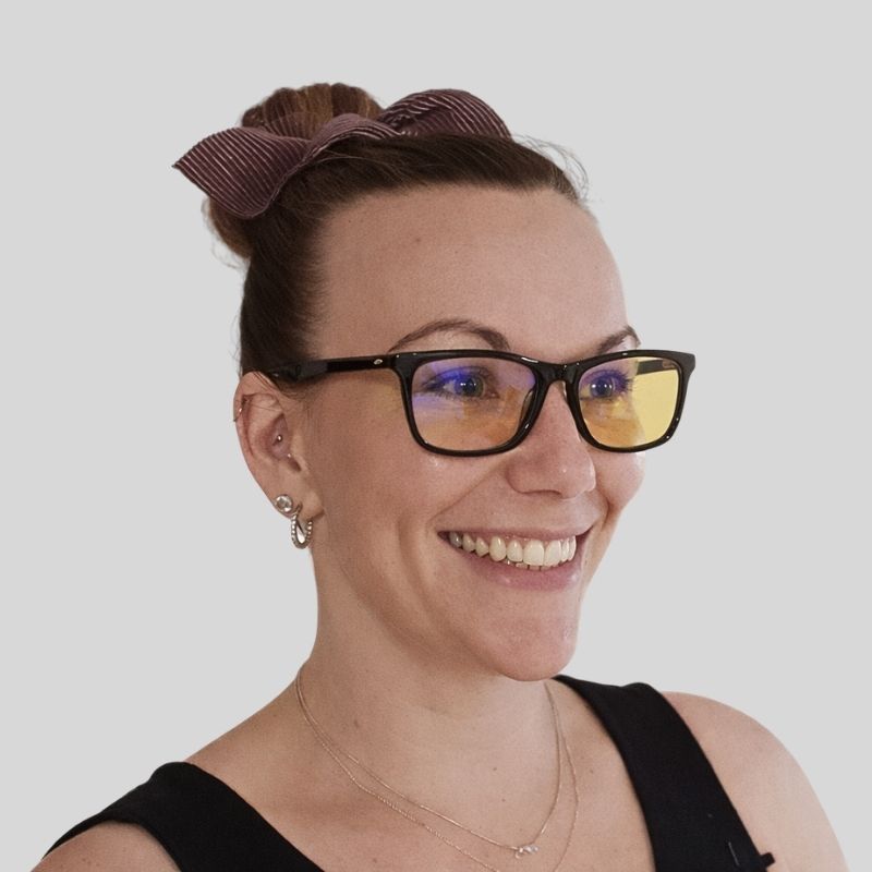 Woman wearing black frame blue light blocking glasses with yellow lenses, shown in a sharp three-quarter studio portrait.