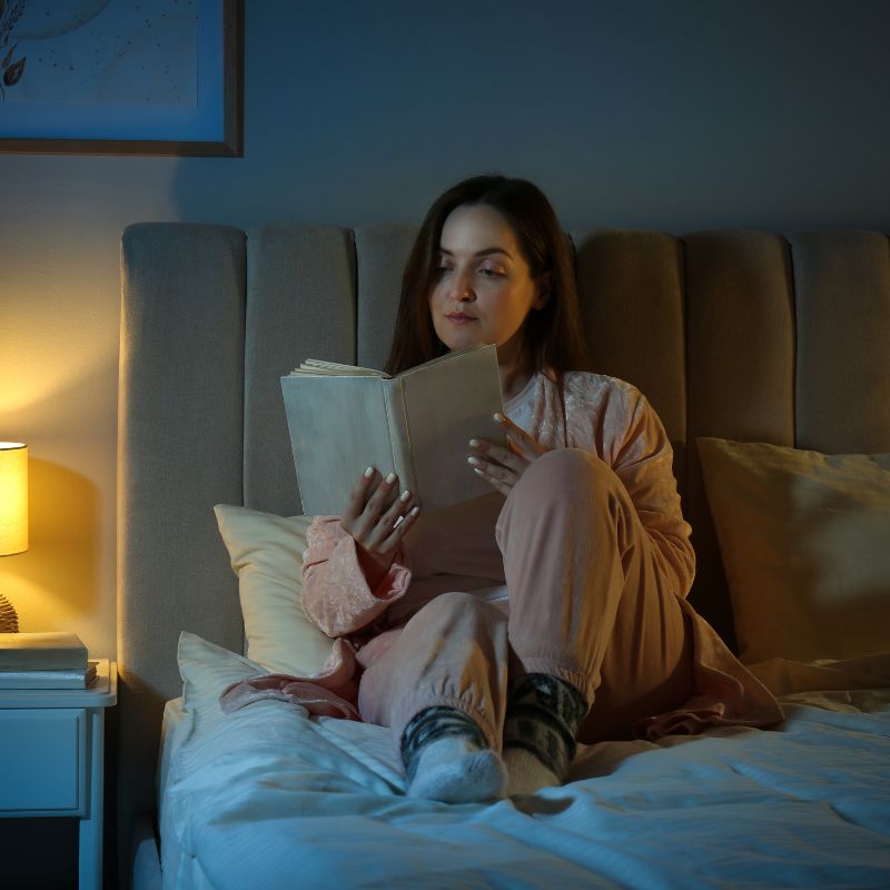 Lady reading book sitting on grounding sheet.