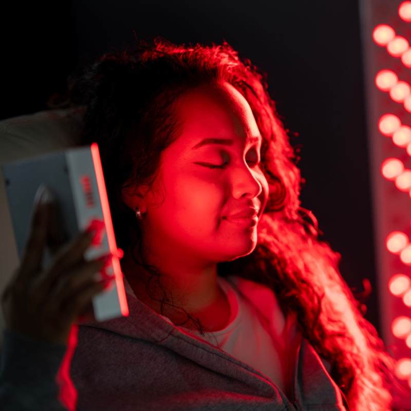 Young women using small red light therapy and infrared panel for face. 