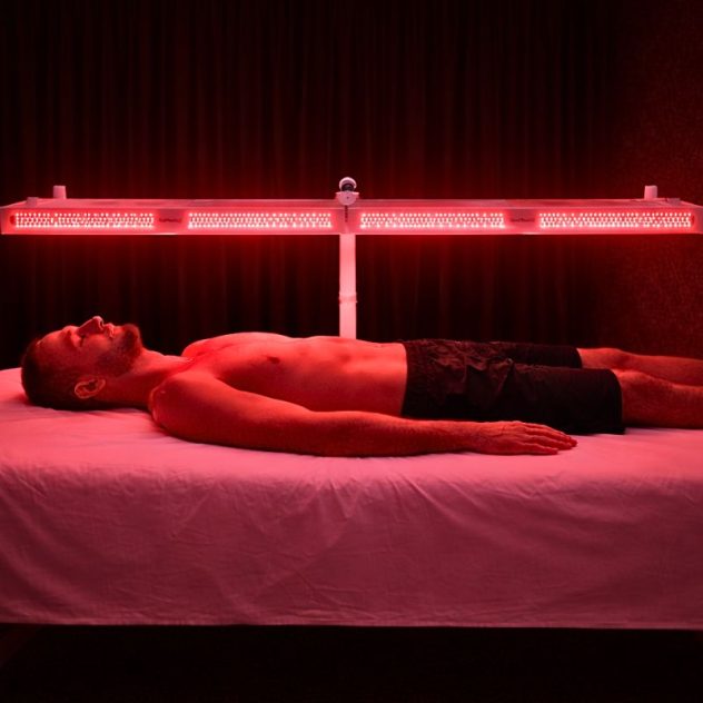 Man using full body red light therapy panel on horizontal stand for muscle recovery.