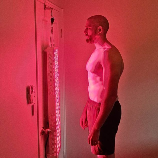 Man using a red light therapy panel hanging on a door for full-body treatment and muscle recovery.