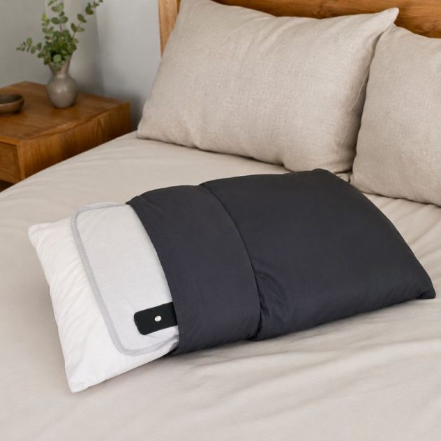 Beige grounding pillow cover fitted over a pillow on a bed with adjustable wrap design and grounding cord beside it